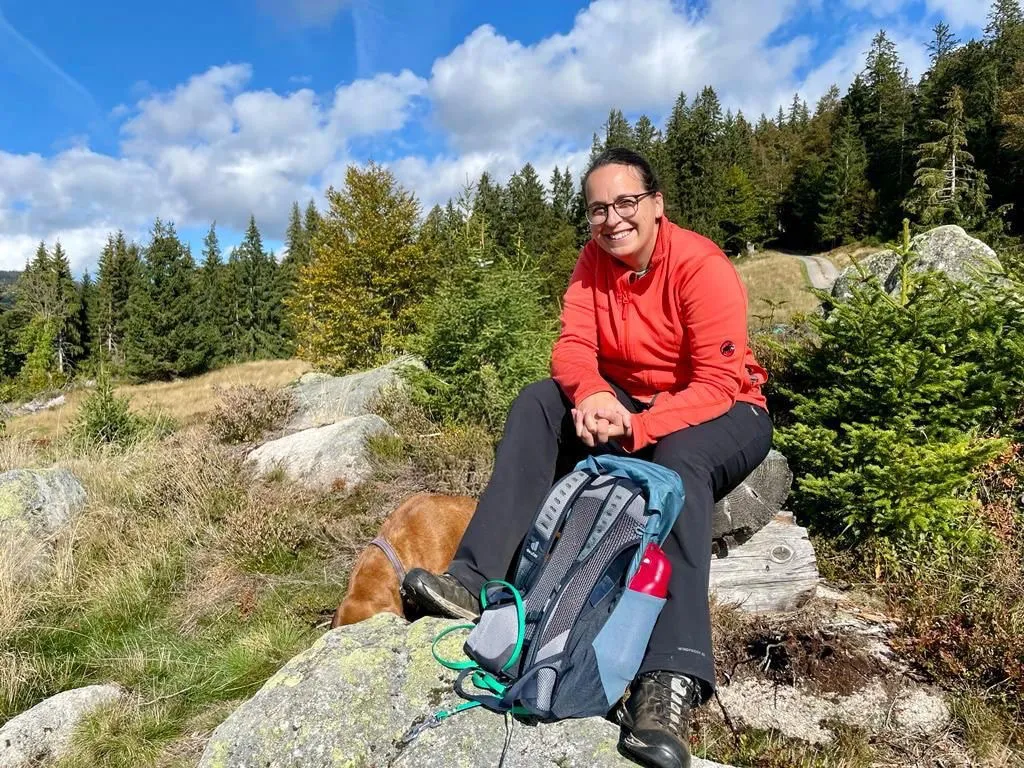 Aline sitzt mit Rucksack auf einem Felsen in der Sonne