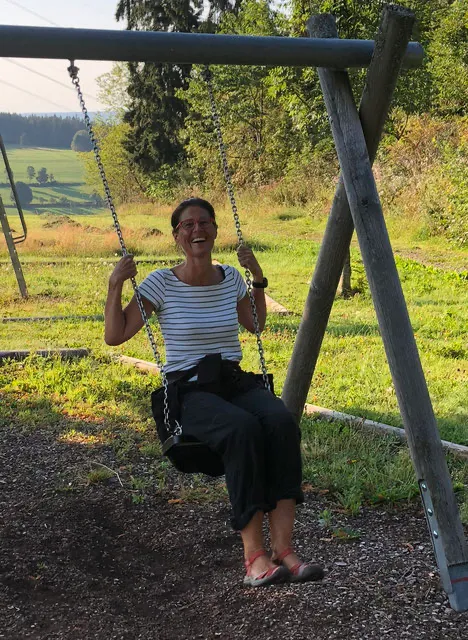Anna sitzt auf einer Holzschaukel im Grünen