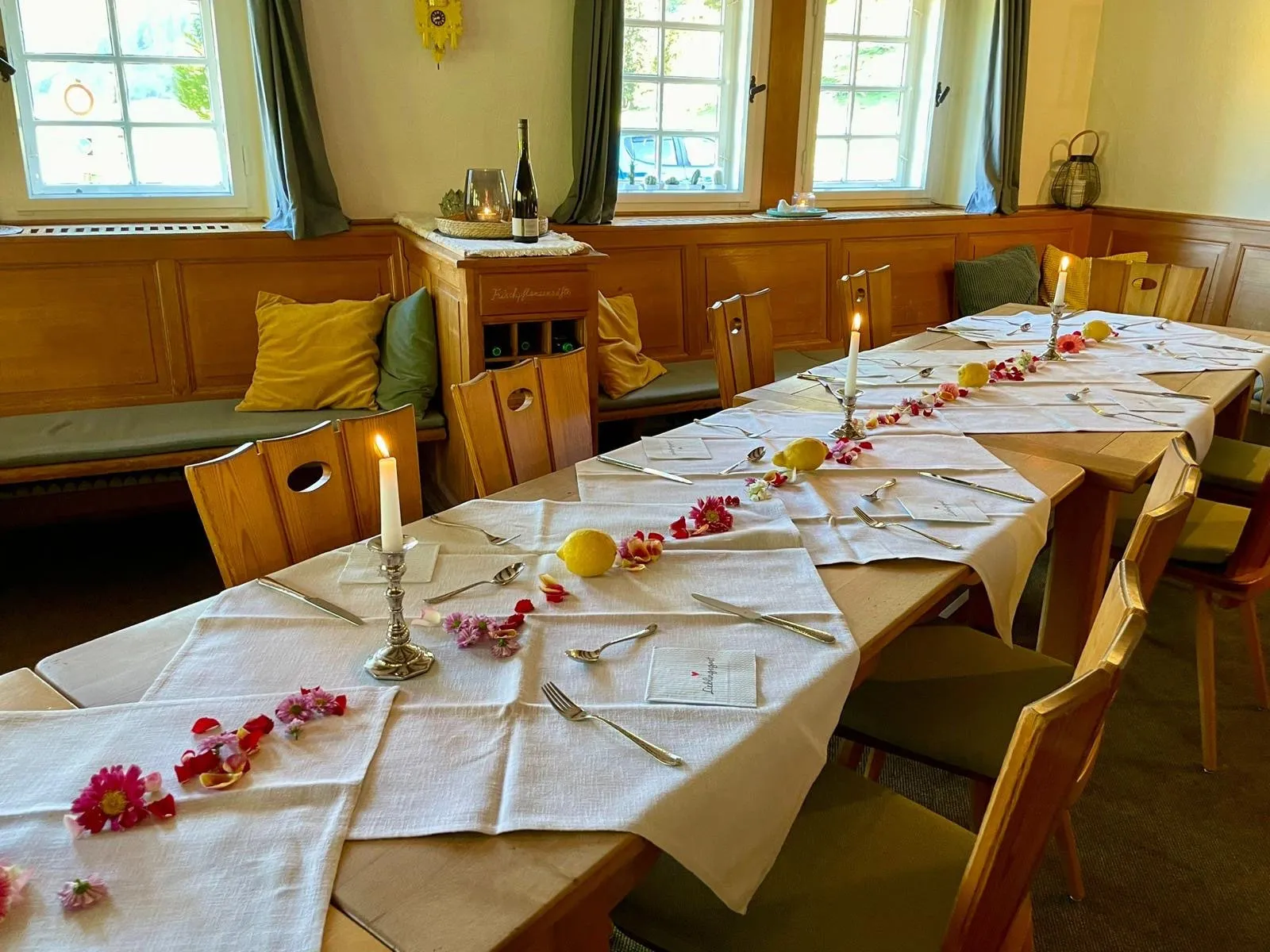 Eine lange Tafel in einer holzgetäfelten Stube, festlich gedeckt mit Kerzen, Zitronen und Blütenblättern