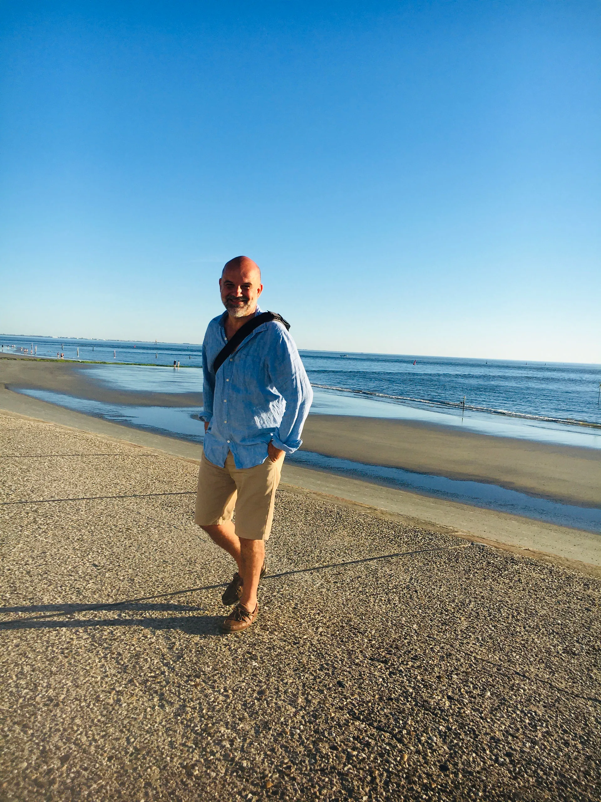 Jens steht in hellblauer Jacke an einem Sandstrand