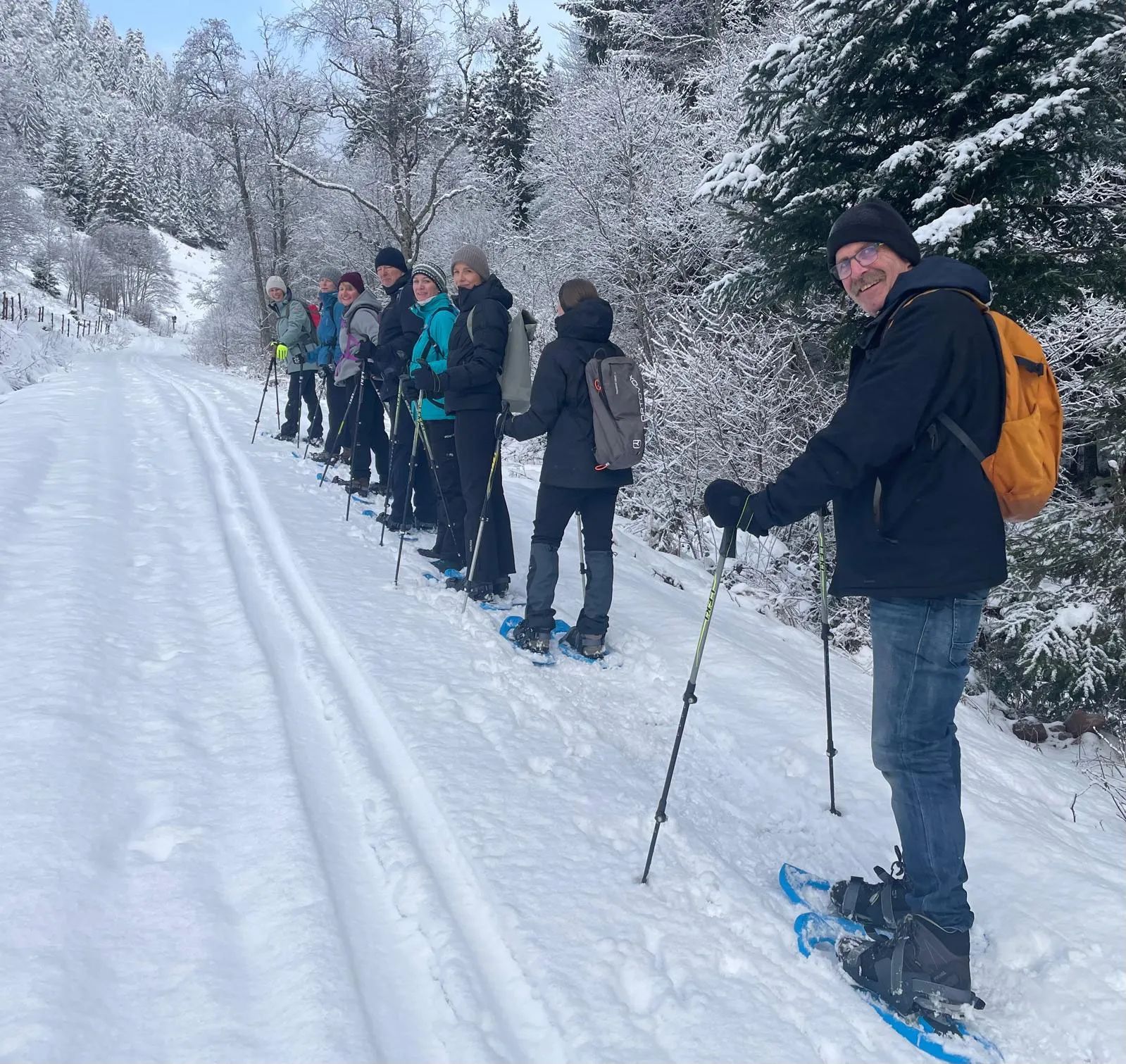 Die Gruppe steht mit Schneeschuhen und Stöcken in einer Reihe auf einem verschneiten Waldweg