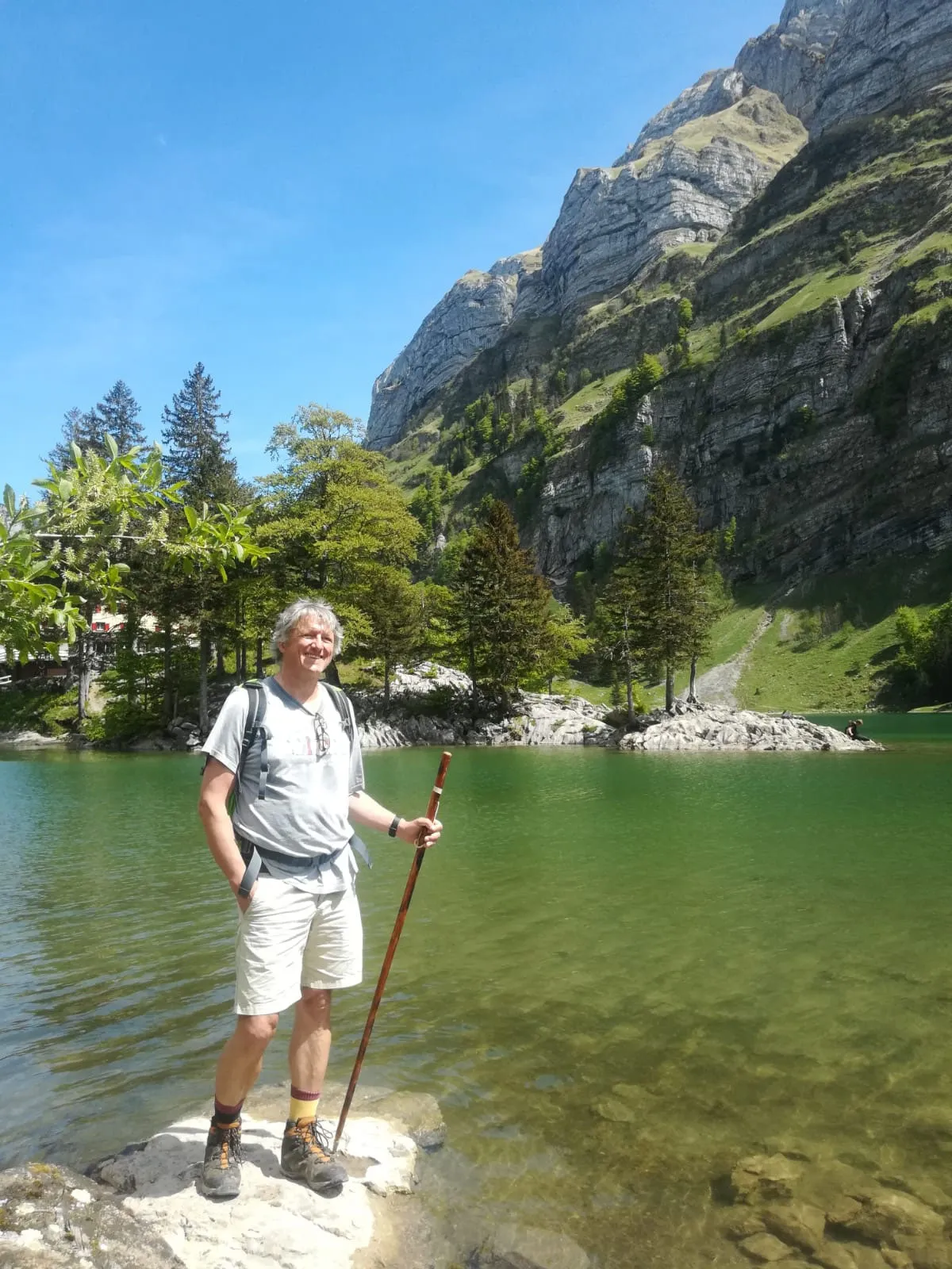 Winfried mit Wanderstock auf einem Stein am Ufer eines Bergsees